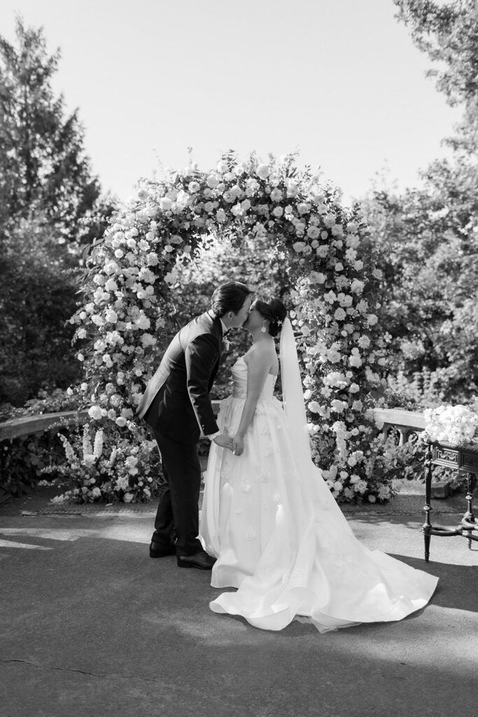 bride and groom kiss in front of arch